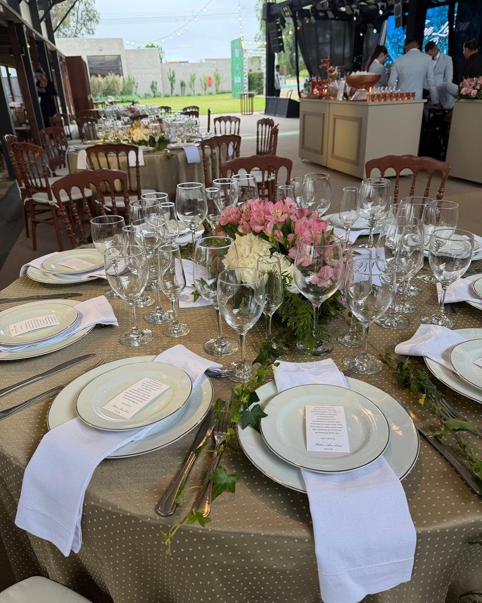 Mesa posta com taças, toalha e flores em evento ao ar livre